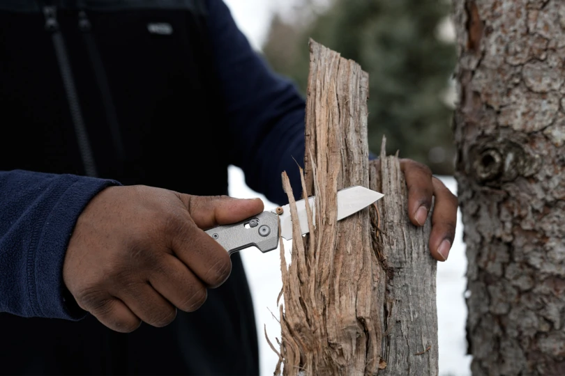 The folding knife being used to carve wood outdoors, held in one hand