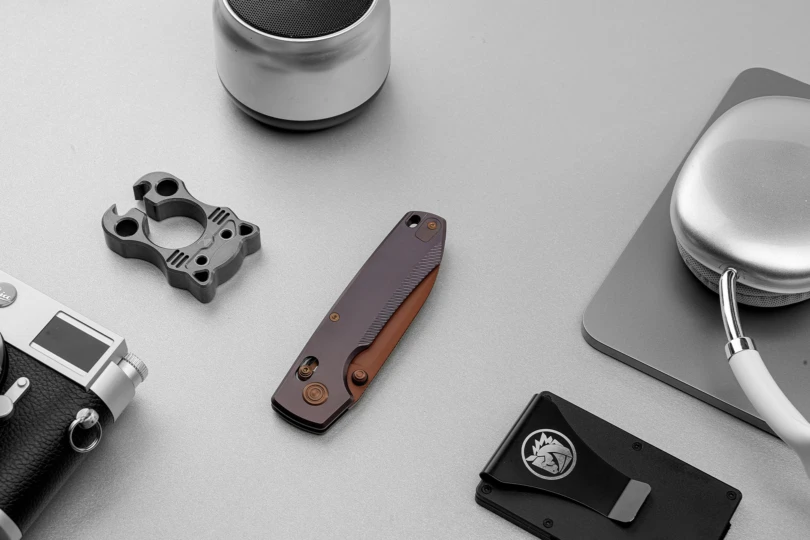 Vosteed Racoon TiSlim folding knife shown closed on a desk with everyday carry items