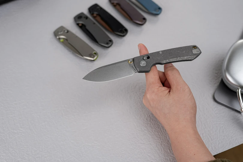 A hand holding an open Vosteed Racoon TiSlim knife, with other slim folding knives in the background