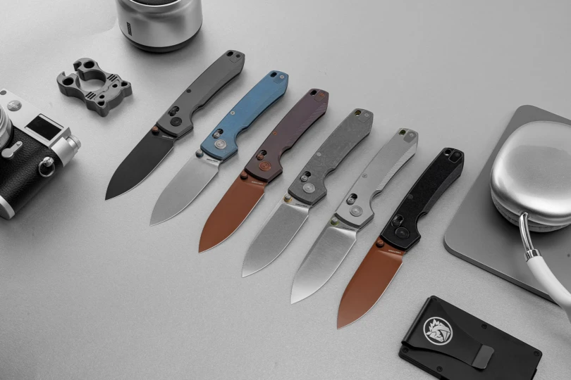 Several Vosteed Racoon TiSlim knives displayed open, showing different handle and blade finishes