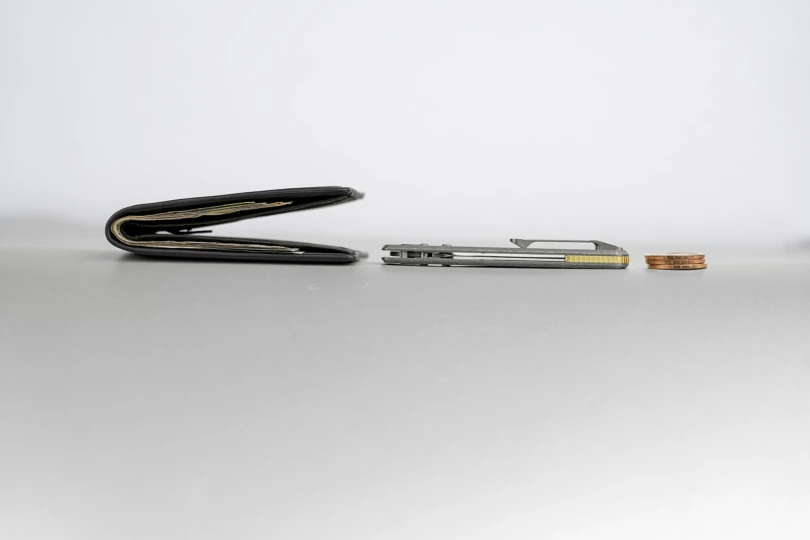 Racoon TiSlim knife placed next to a wallet and coins to show slim carry profile