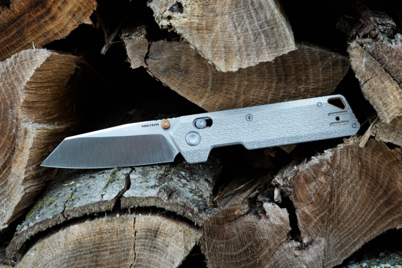 The Vosteed Parallel folding knife resting open on a stack of cut firewood