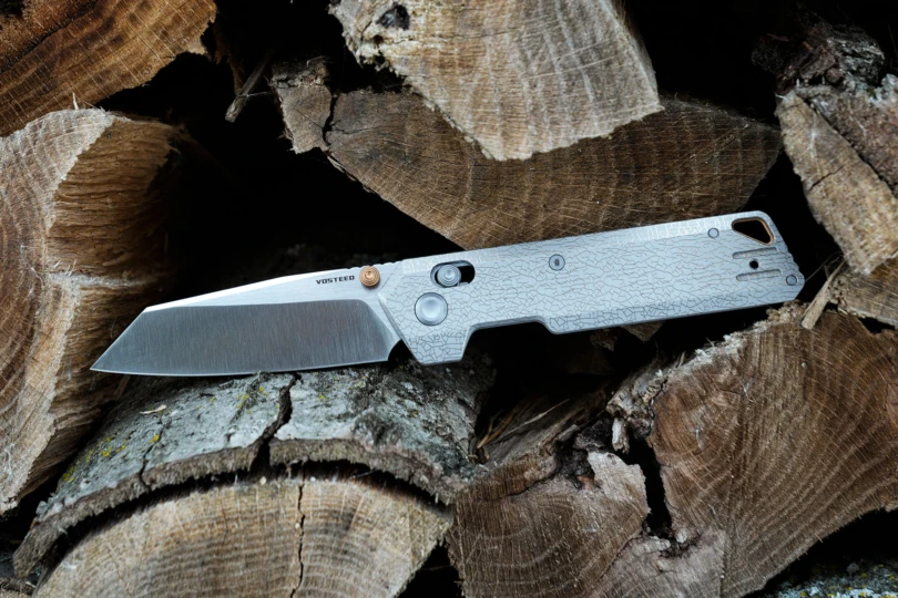 The Vosteed Parallel folding knife resting open on a stack of cut firewood