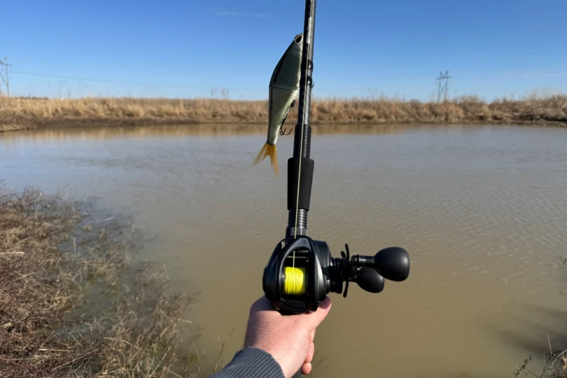 The Abu Garcia Beast Baitcasting Combo is held over a small pond with a swimbait lure hanging from the rod tip