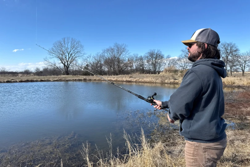 The Beast baitcasting combo is used from the shoreline of a calm pond on a clear day