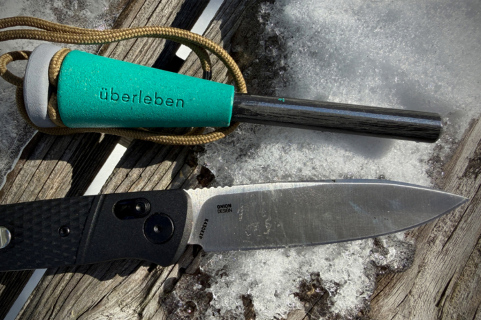 The CRKT folding knife placed on snow next to a ferro rod and cord