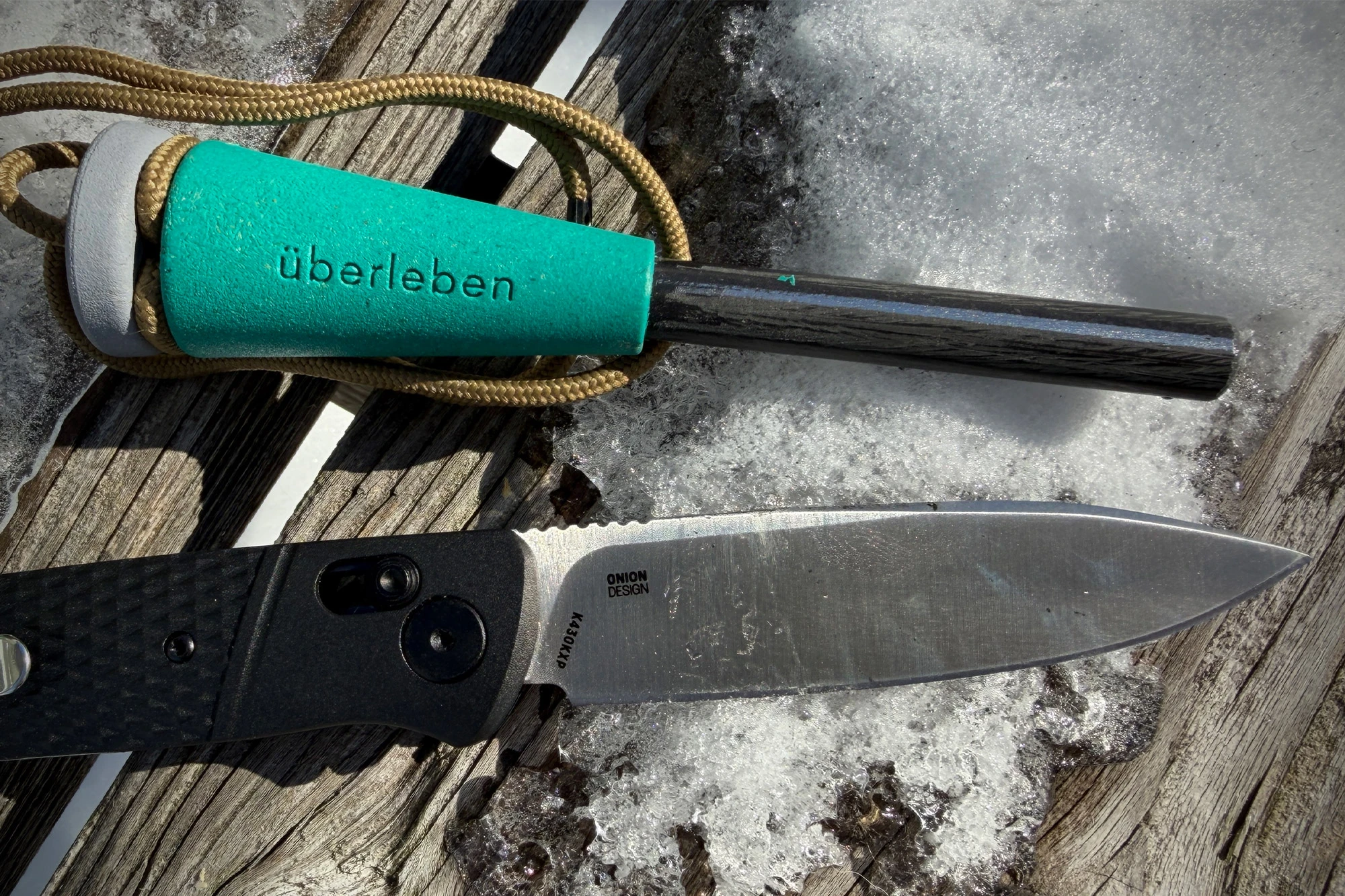 The CRKT folding knife placed on snow next to a ferro rod and cord