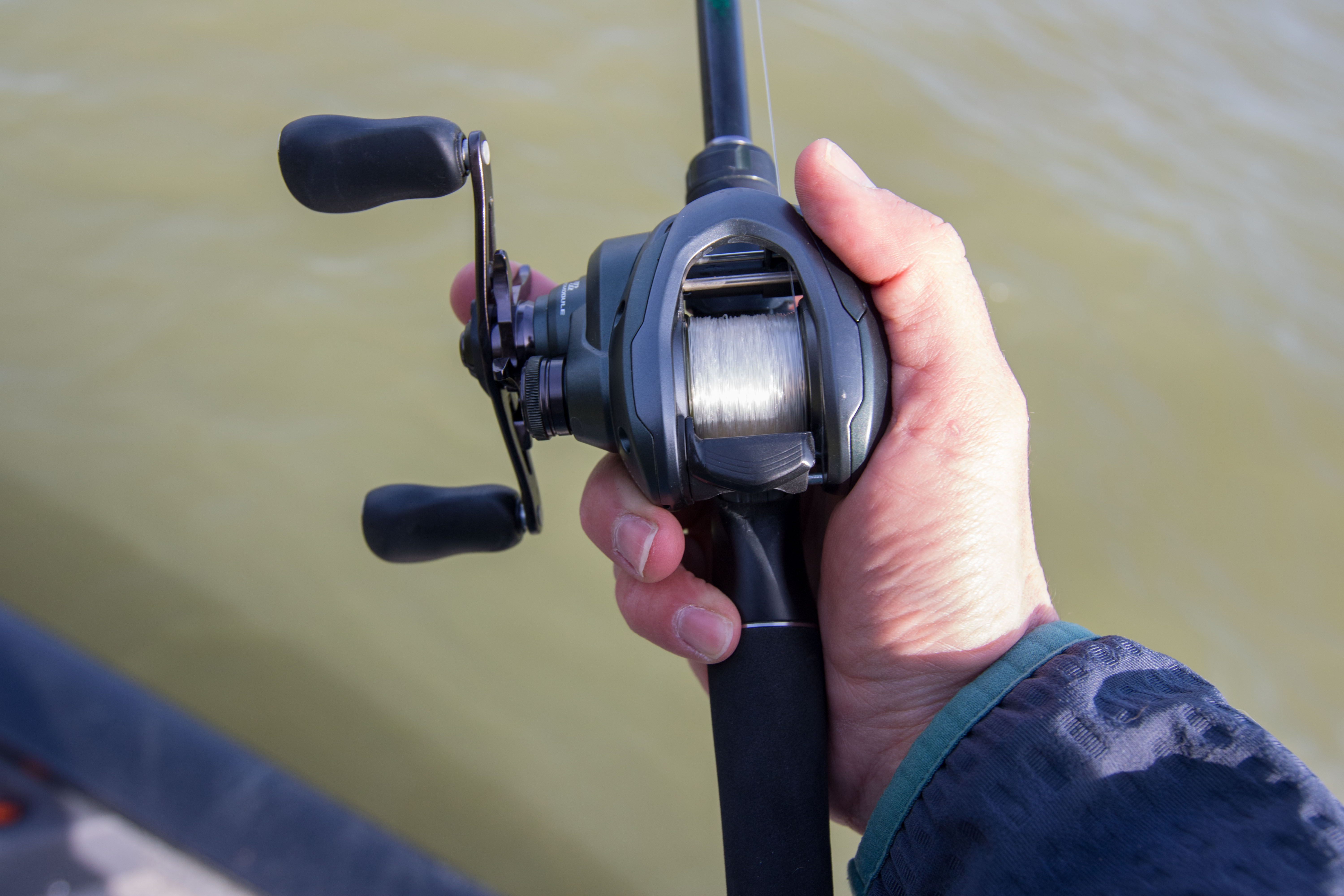 An anglers hand palming a bass fishing reel.