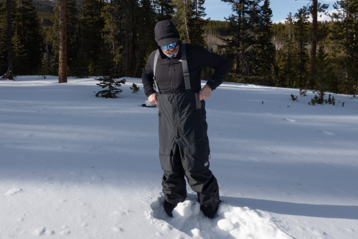 A full-body view showing the fit of the REI Co-op First Chair bibs while standing in deep snow