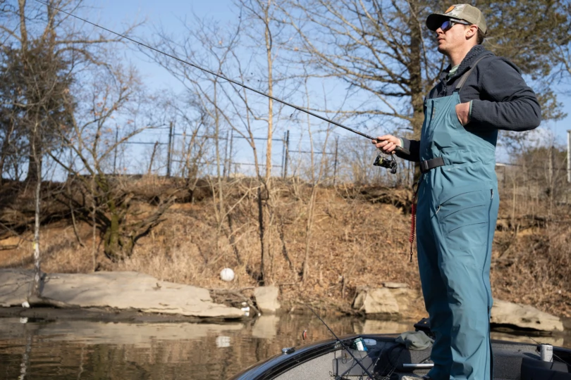 A fisherman on a boat deck fishing with a spinning rod.