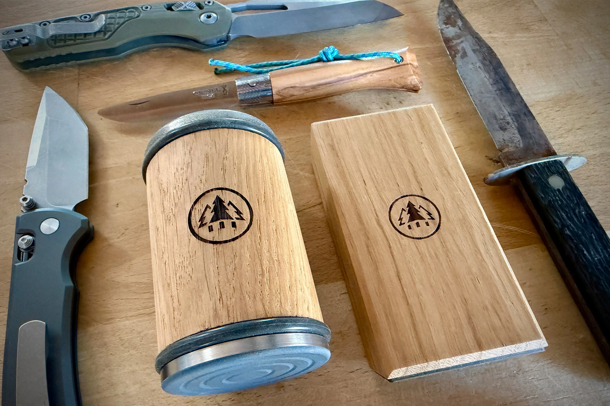 The rolling sharpener and angle block are placed among several knives on a wooden table