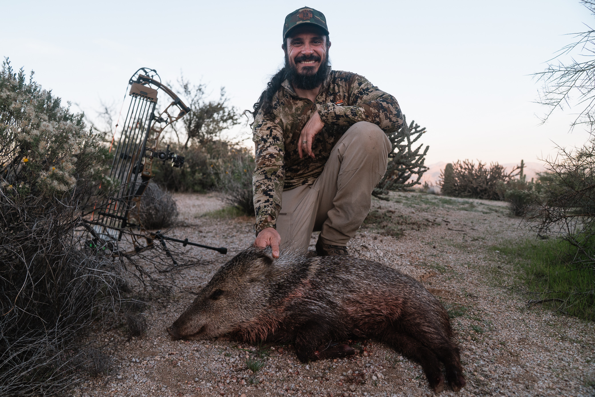 A hunter kneels beside harvested game with a compound bow equipped with the Hamskea R7 Arrow Rest