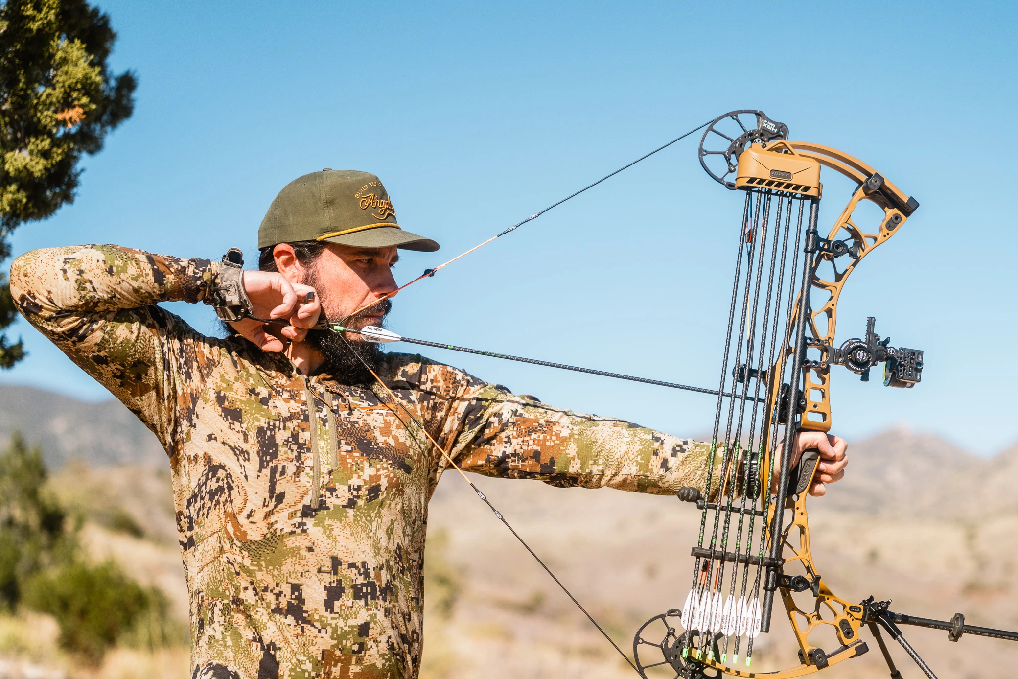 A hunter holds a compound bow at full draw with the Hamskea R7 Arrow Rest supporting the arrow