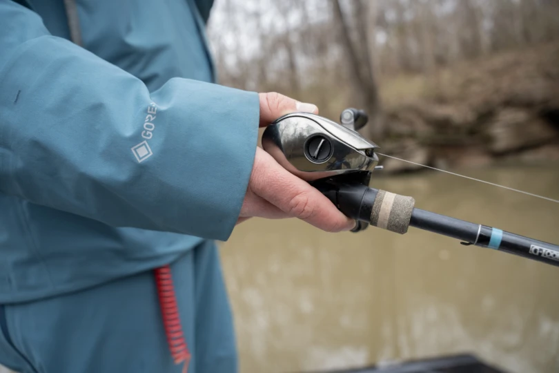 A close shot of a hand holding a fishing rod and bait caster.