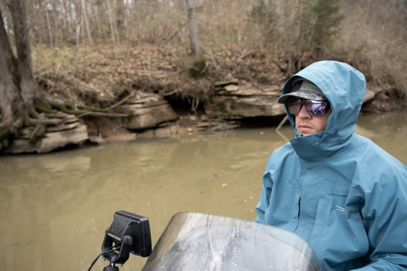 A man driving a boat with the SITKA Cat 5 jacket on.