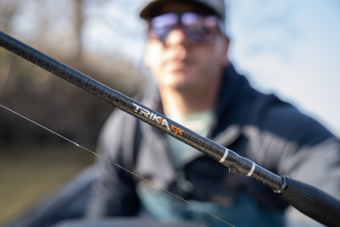 A closeup shot of the Trika 10X rod label with an anglers face blurred in the background.