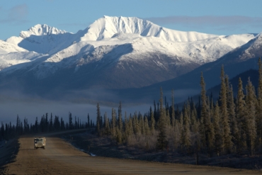 snow capped mountains with forest and road with truck below