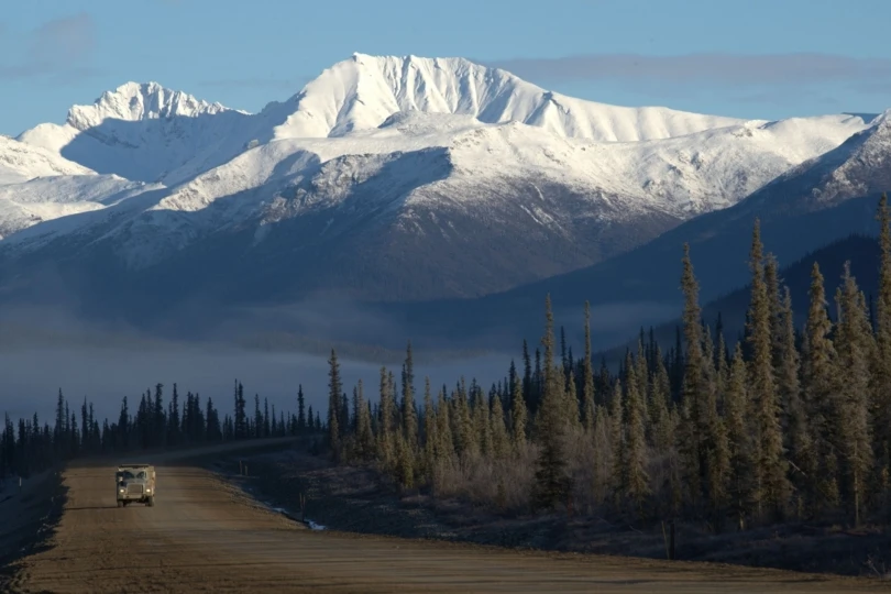 snow capped mountains with forest and road with truck below