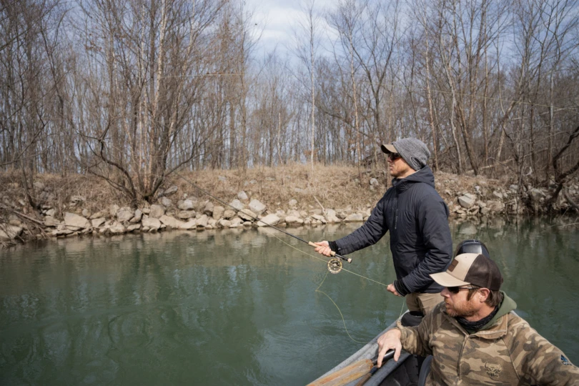 An angler casting a fly rod in a drift boat on a southern bass river.