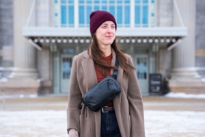 woman stands outside hotel building wear coat and sling bag