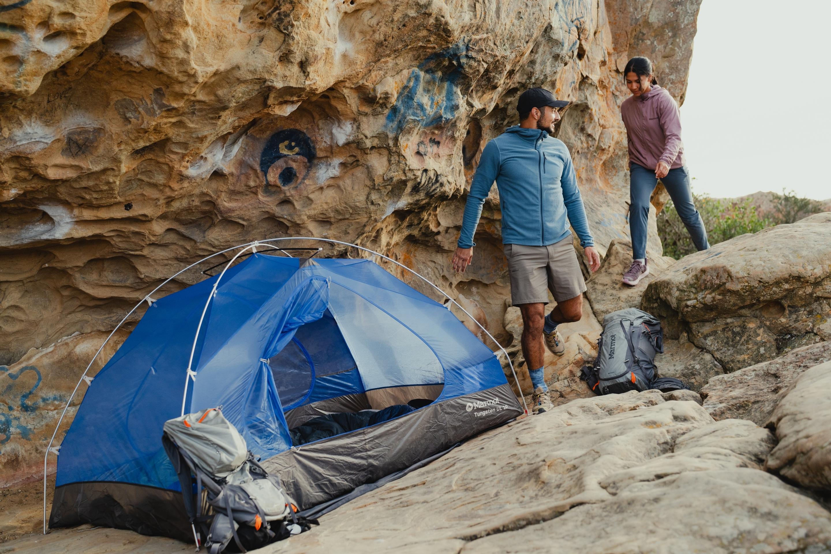 people walk by set-up tent in rocky area
