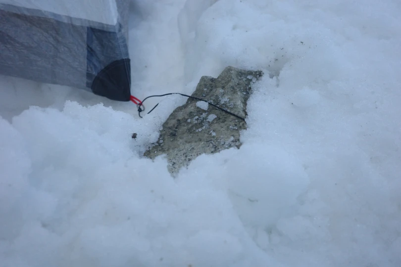 Tent anchored in snow using a rock and cord system