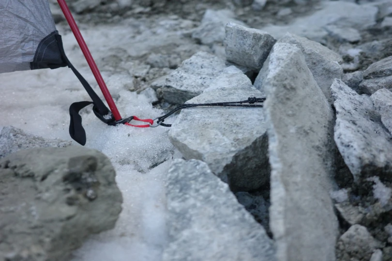 Tent guyline secured around rocks on icy ground for stability