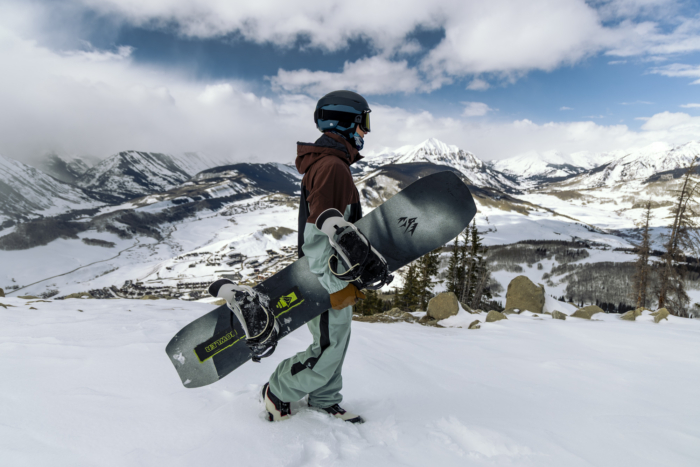 Snowboarder carries the Jones Howler across a snowy ridge with wide mountain views