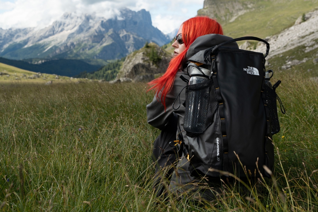 view from behind of woman sitting in meadow wearing backpack