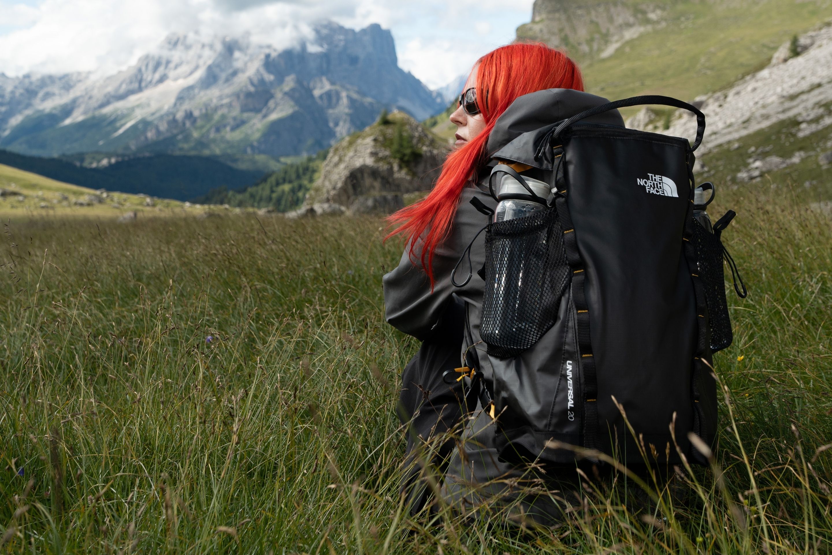 view from behind of woman sitting in meadow wearing backpack