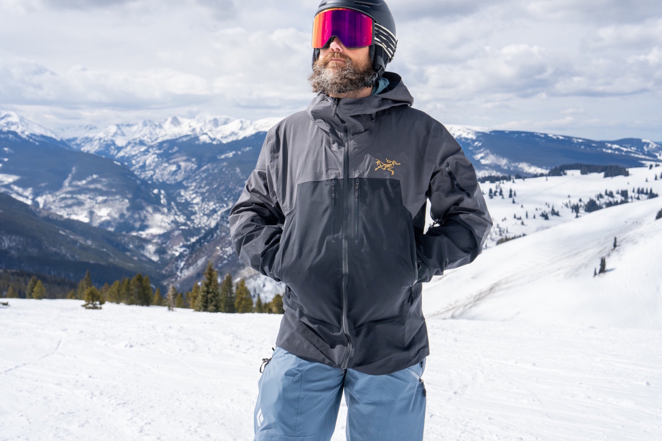 A skier standing on a snowy ridge wearing the Arc'teryx Rush jacket