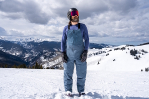 Skier wearing blue Black Diamond Recon Stretch Bibs standing on a snowy mountain ridge