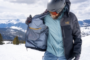 Skier wearing Black Diamond Recon Bibs opening a ski jacket to show inner layering