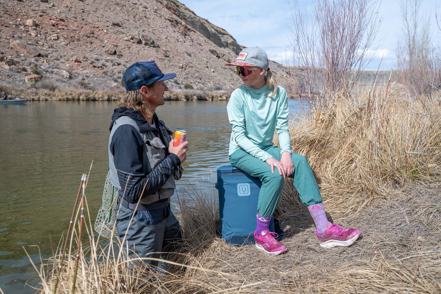 A person sitting on top of the BrüMate MagPack cooler next to a river