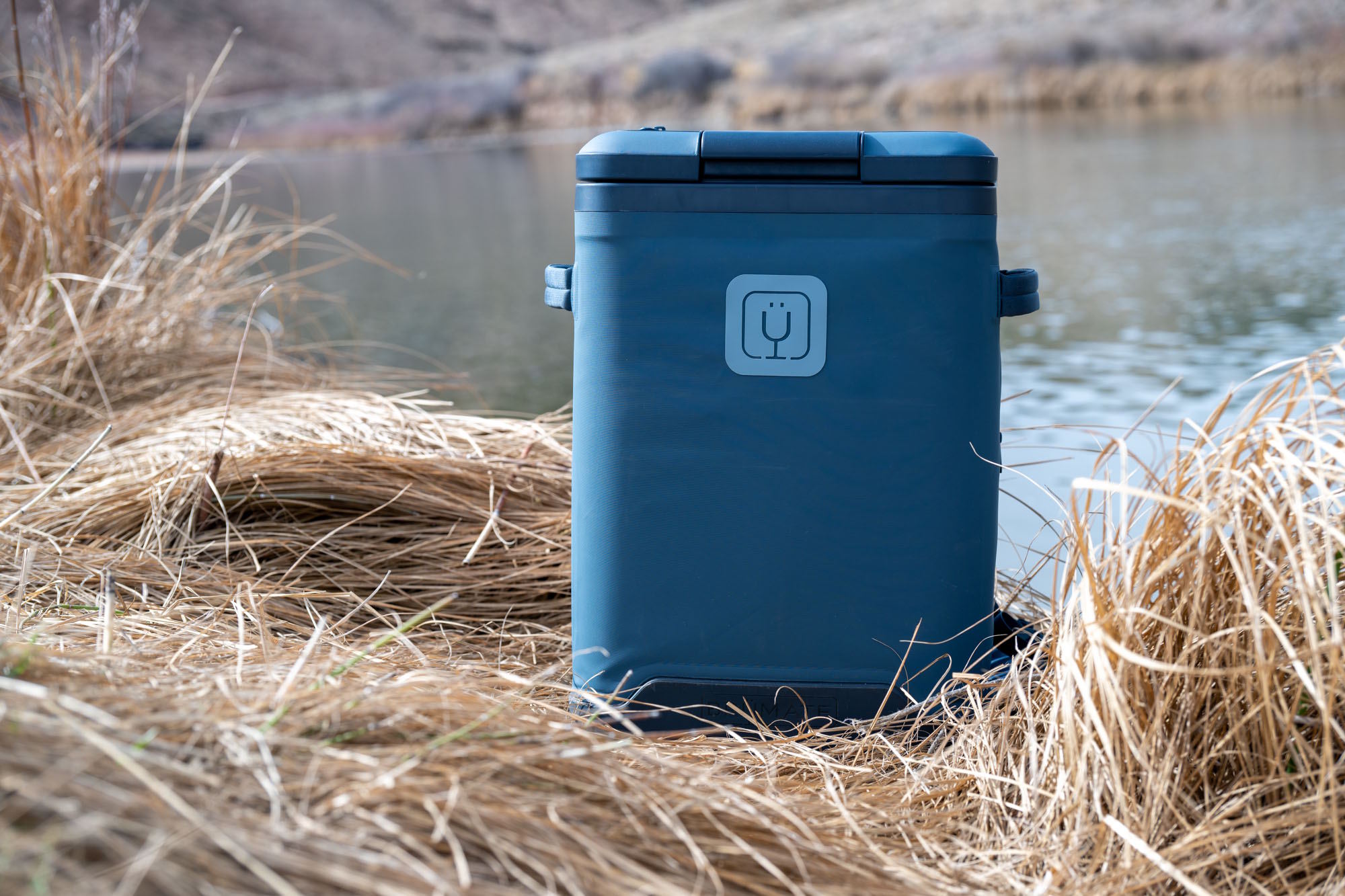 Blue BrüMate MagPack 24-can cooler backpack standing in tall dry grass.