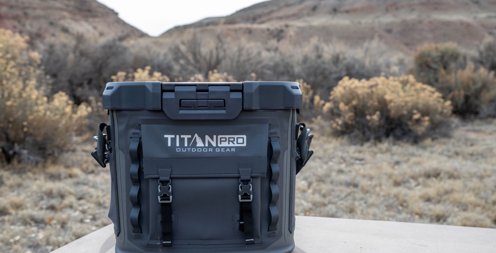 Titan Pro outdoor gear cooler box placed on a table in a dry desert landscape with hills in the background