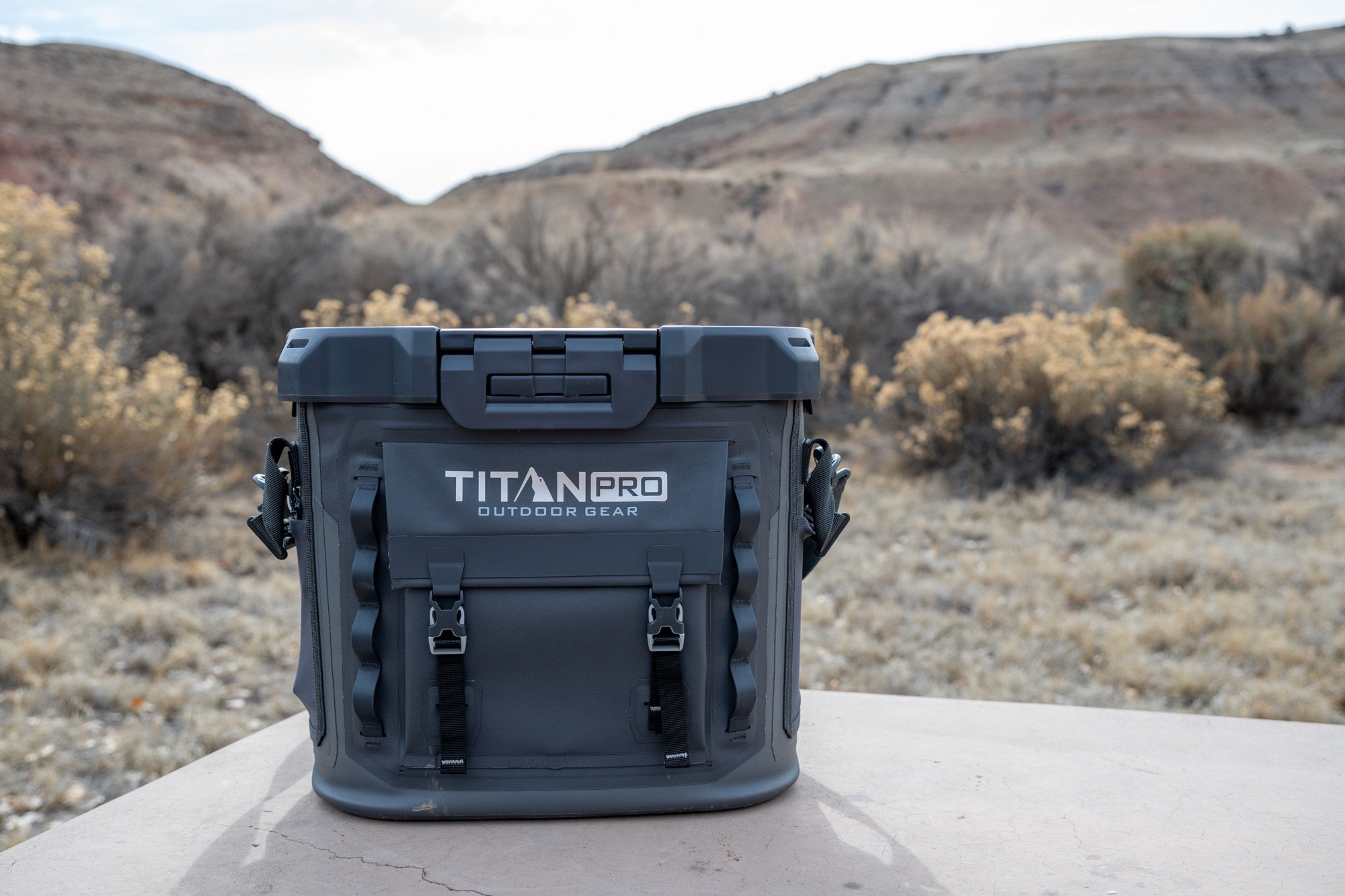 Titan Pro outdoor gear cooler box placed on a table in a dry desert landscape with hills in the background