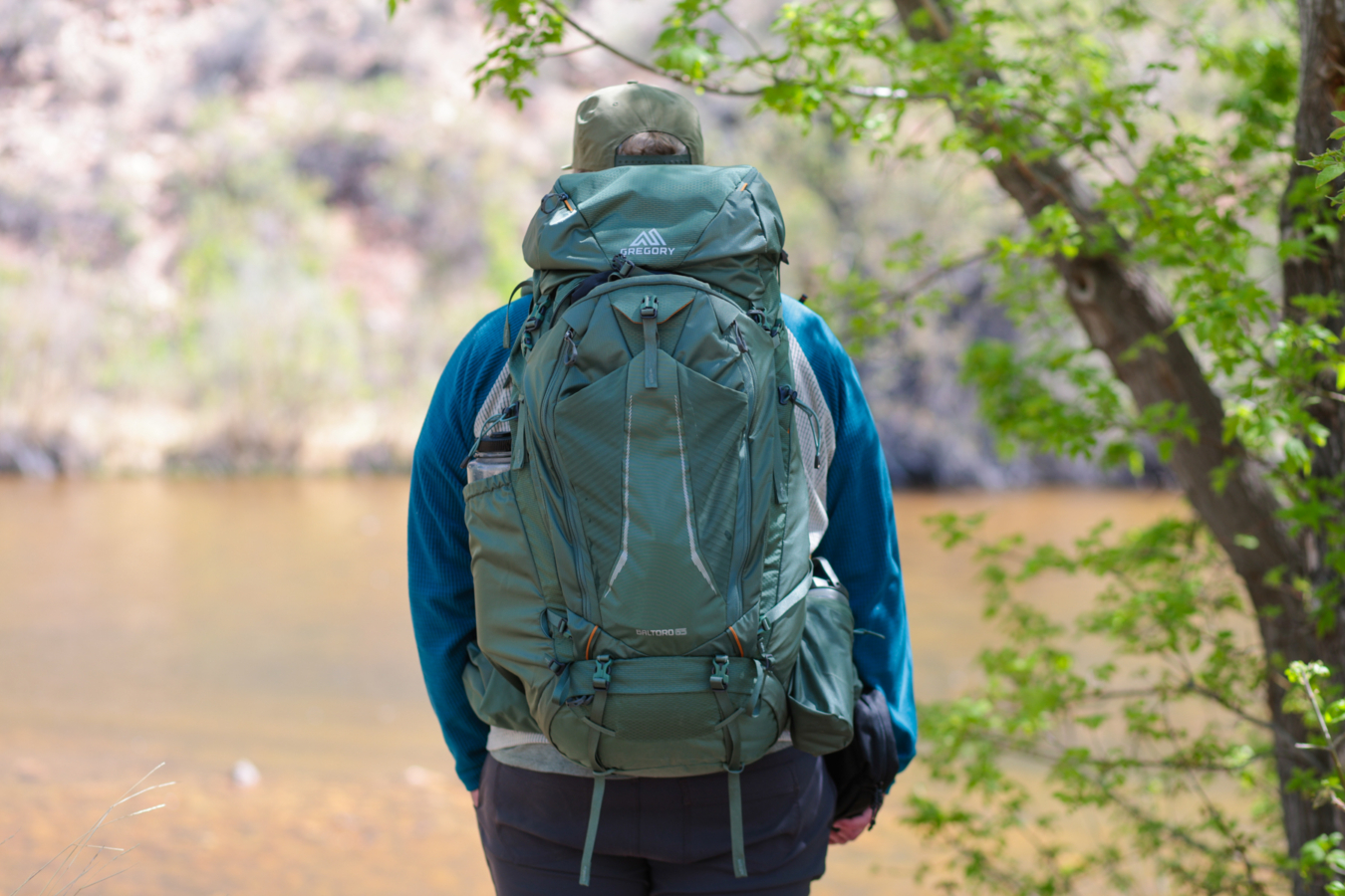 A hiker wears the Gregory Baltoro 65 backpack while standing beside the water