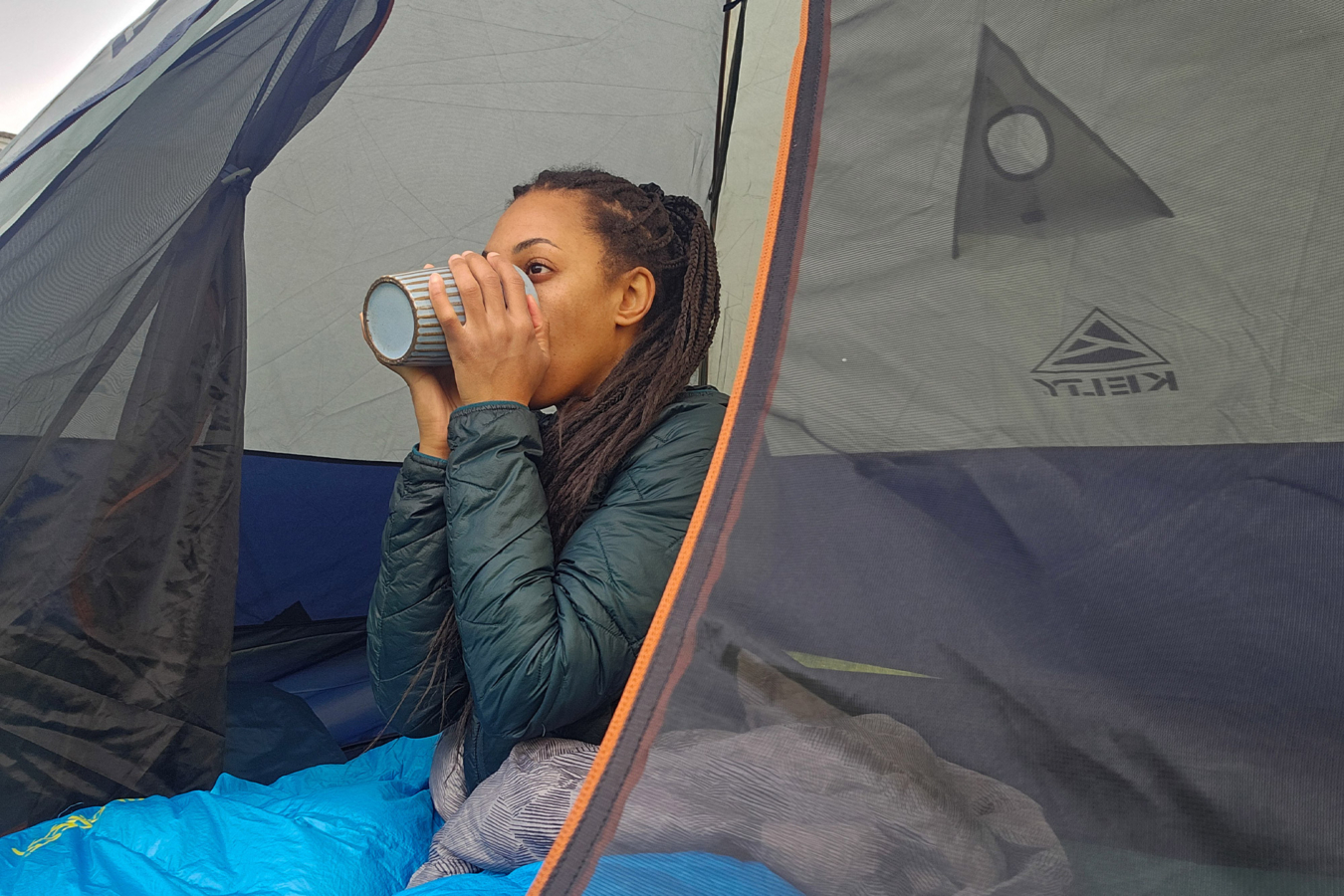 A camper sits inside the Kelty tent with the mesh door open