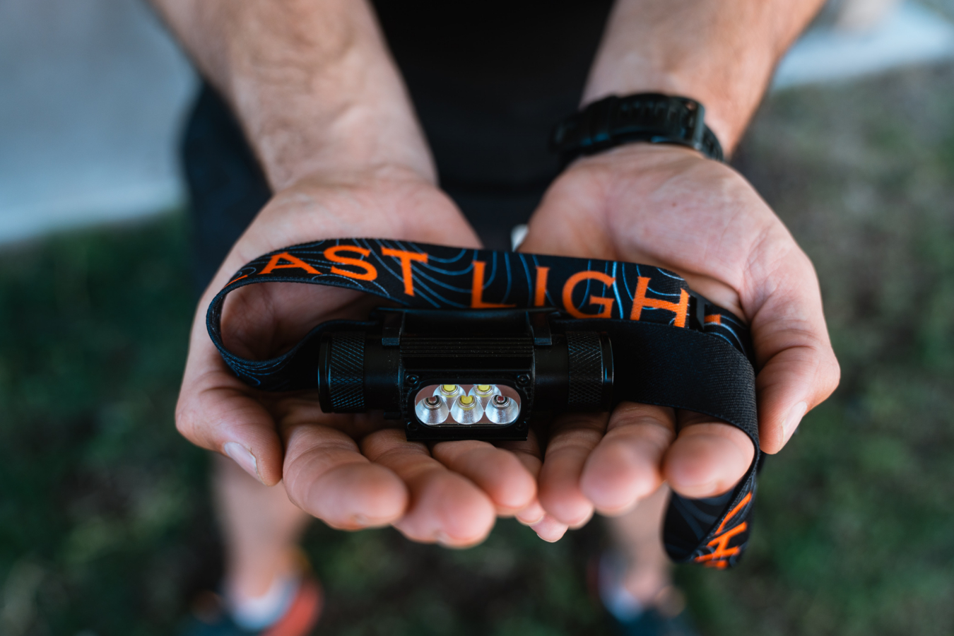 A person holds the Last Light headlamp with the front LEDs and strap visible