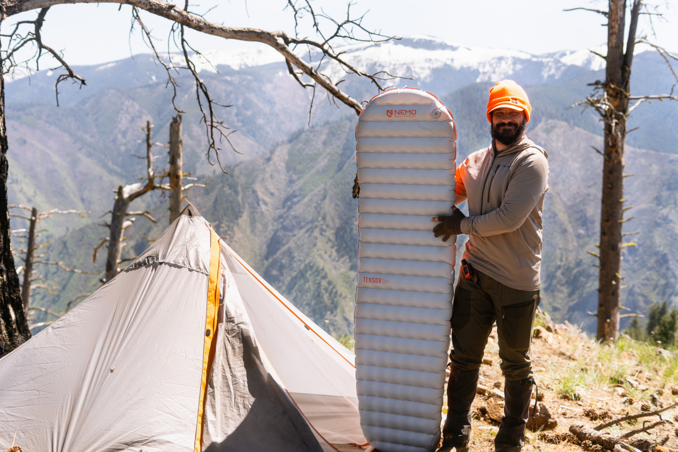 NEMO Tensor sleeping pad held upright beside a tent at a mountain campsite