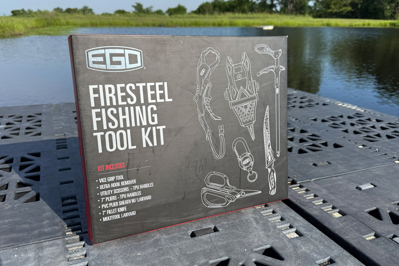 The EGO FireSteel Fishing Tool Kit box sits on a black dock beside a pond, with illustrated tools and the included kit items shown on the front
