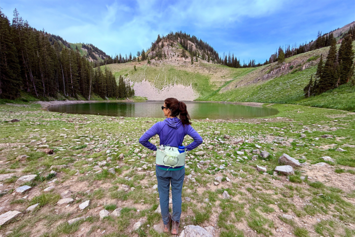 A hiker in a purple Echo Hoodie stands by an alpine lake