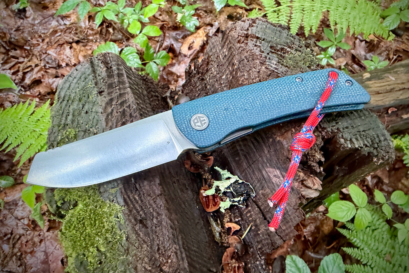 Open Flavorist knife with teal handle and red lanyard angled on a mossy stump