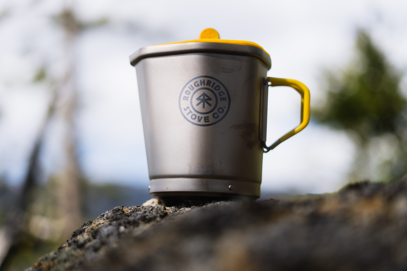 The Roughridge cook pot sits on a rock with its yellow lid and handle visible