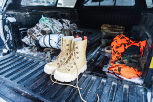 Bunny Boot Lite boots sit in the snowy bed of a pickup truck with hunting gear and orange safety clothing nearby