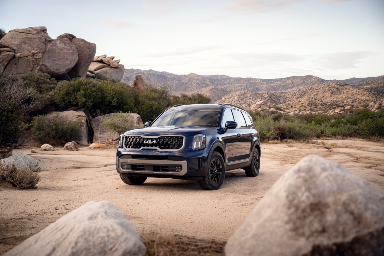 A blue 2023 Kia Telluride SUV is parked next to a big pile of rocks in the desert.