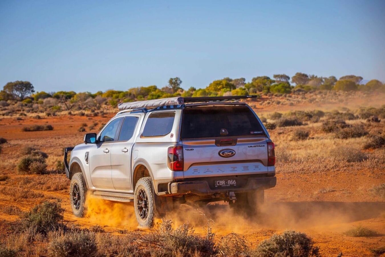 A silver Ford Ranger drives through the desert with an ARB truck cap installed.