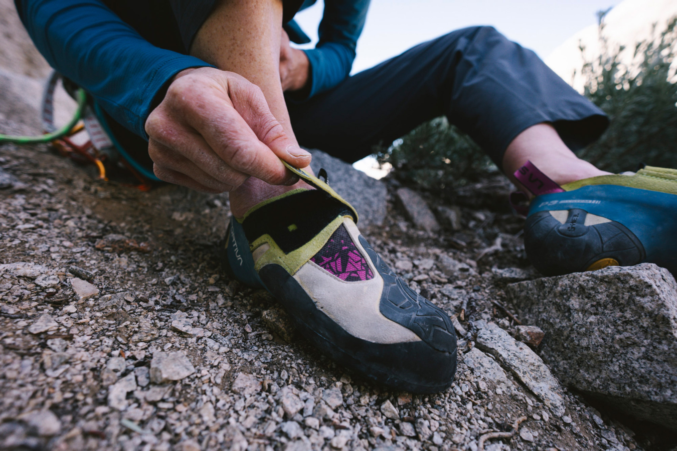 Climber adjusting a La Sportiva Skwama shoe on rocky ground before climbing