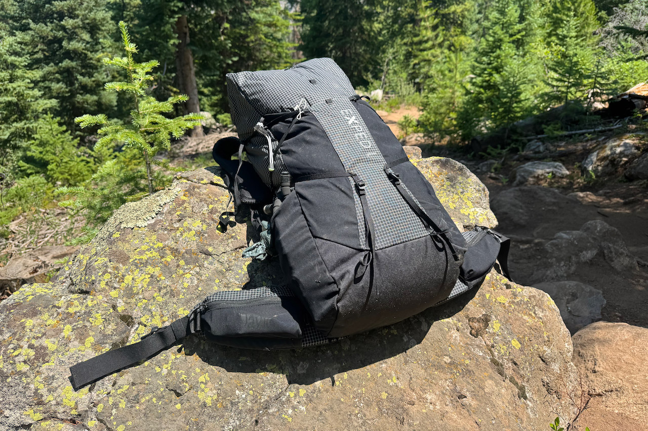 Black 50-liter hiking backpack resting on a rock beside a forest trail